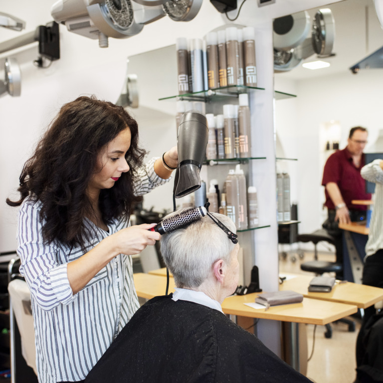 Friseurin mit Behinderung föhnt einem Kunden die Haare