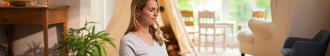 Junge Frau im Yoga-Sitz auf Yoga-Matte im Wohnzimmer