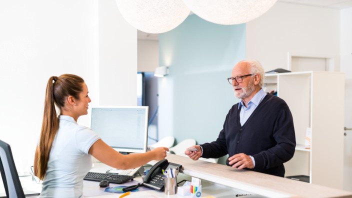 Sprechstundenhilfe reicht einem Patienten seine Versichertenkarte