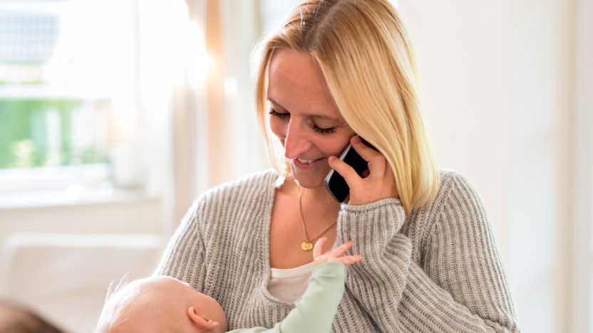 Mutter mit Baby auf dem Arm informiert sich telefonisch mit IKK Med