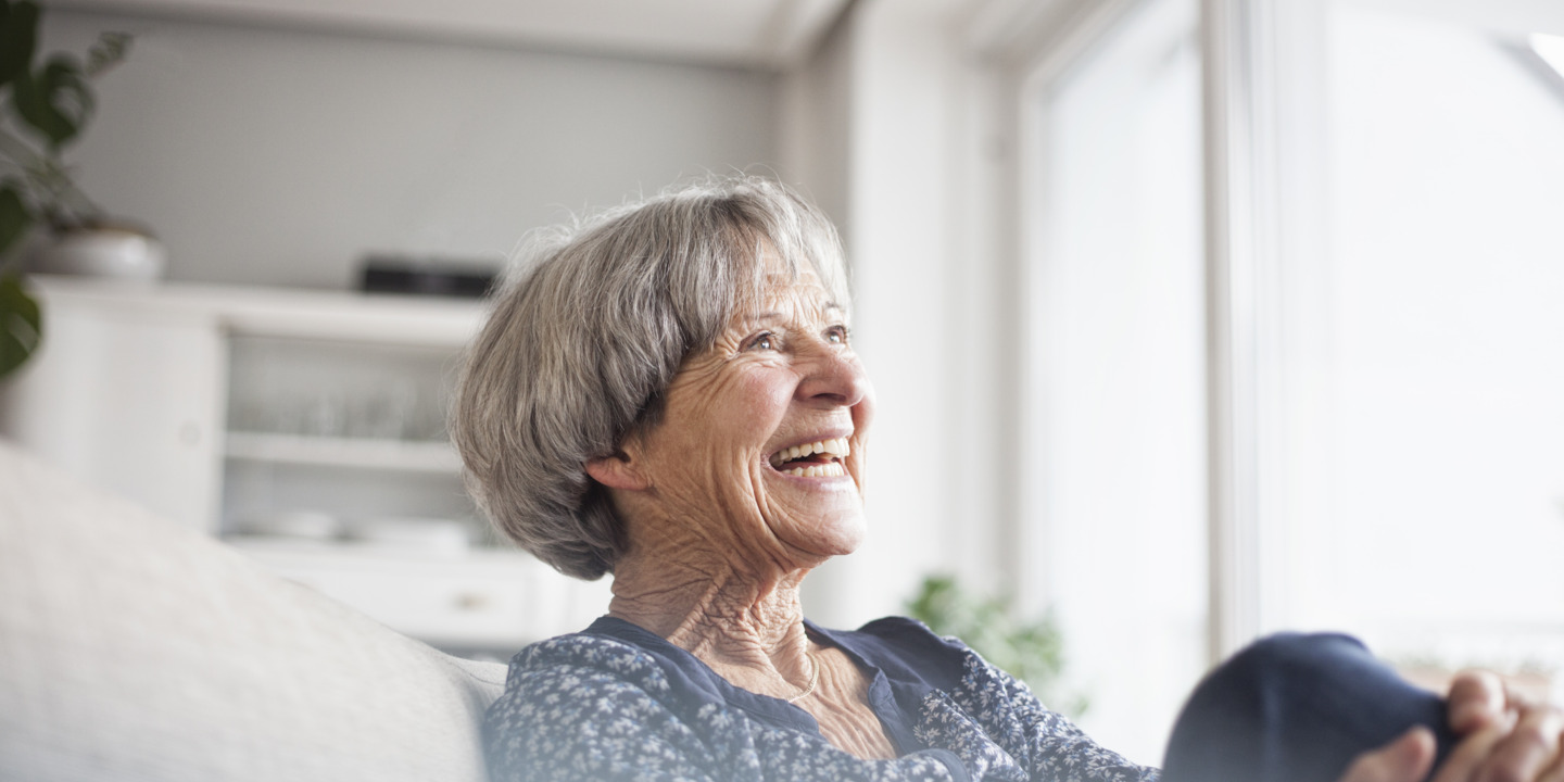 Seniorin sitzt gut gelaunt auf ihrer Couch