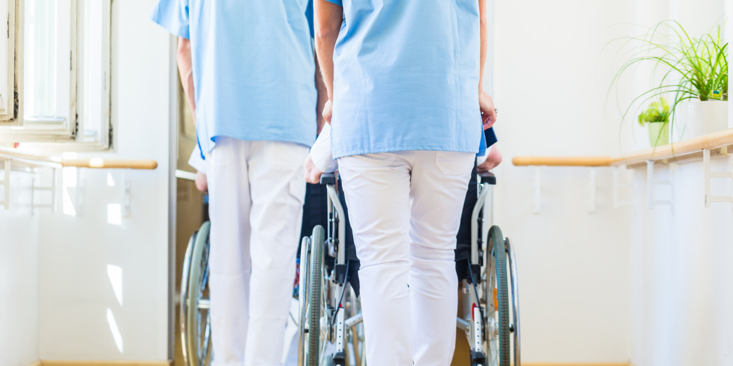 Krankenhausmitarbeiter schieben zwei Patienten im Rollstuhl