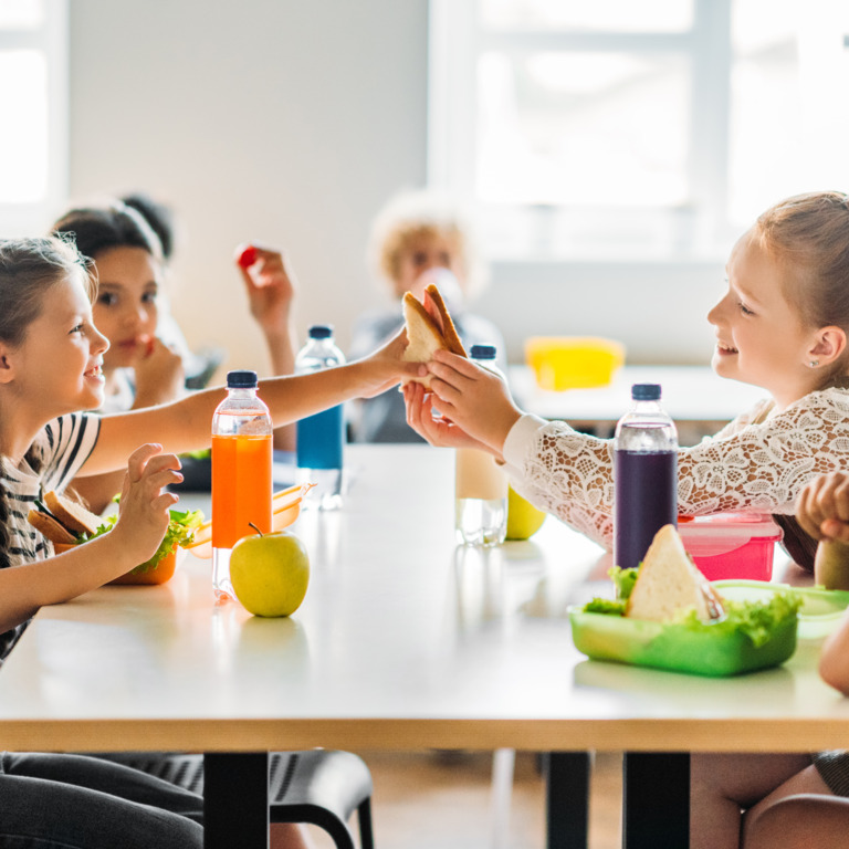 Grundschulkinder sitzen während der Frühstückspause gemeinsam am Tisch