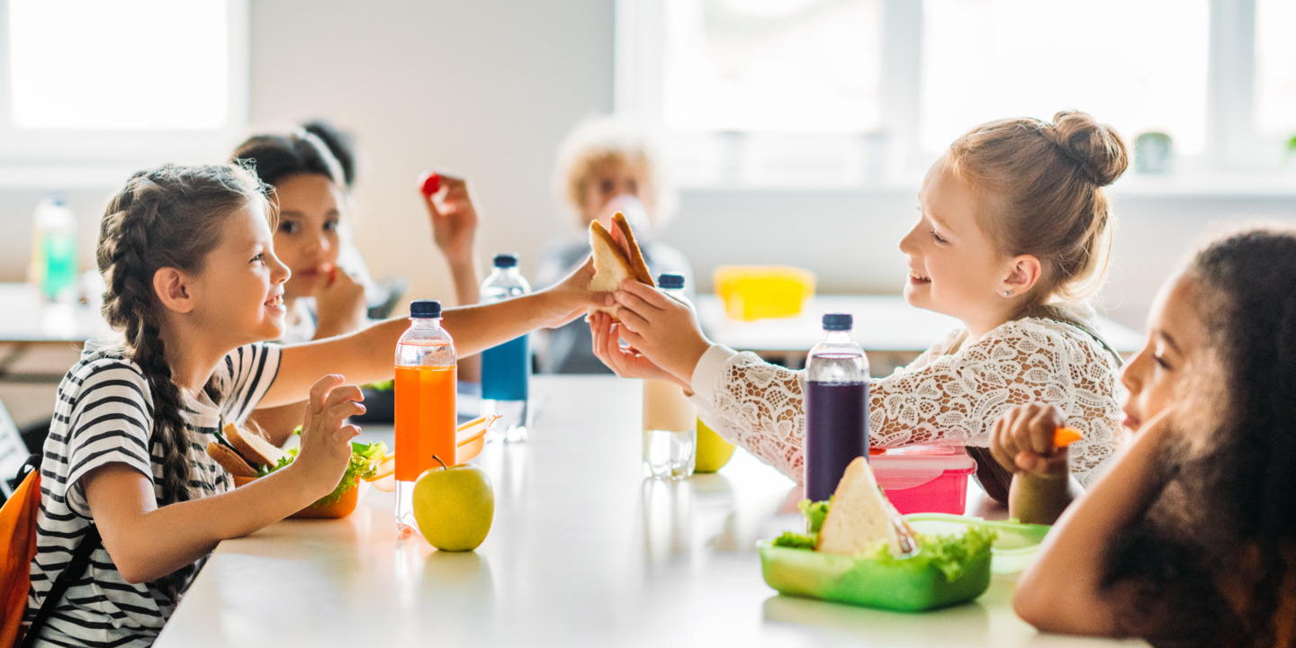 Schulkinder sitzen in der Pause an einem Tisch und essen Brote