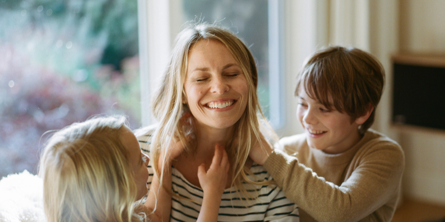 Junge Mutter sitzt lachend mit Kindern auf dem Sofa