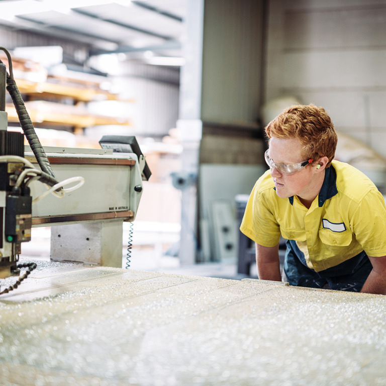 Junge Person mit Schutzbrille steht an Arbeitsgerät.