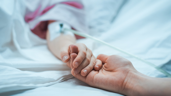 Erwachsene Hand hält Kinderhand mit Infusion im Arm