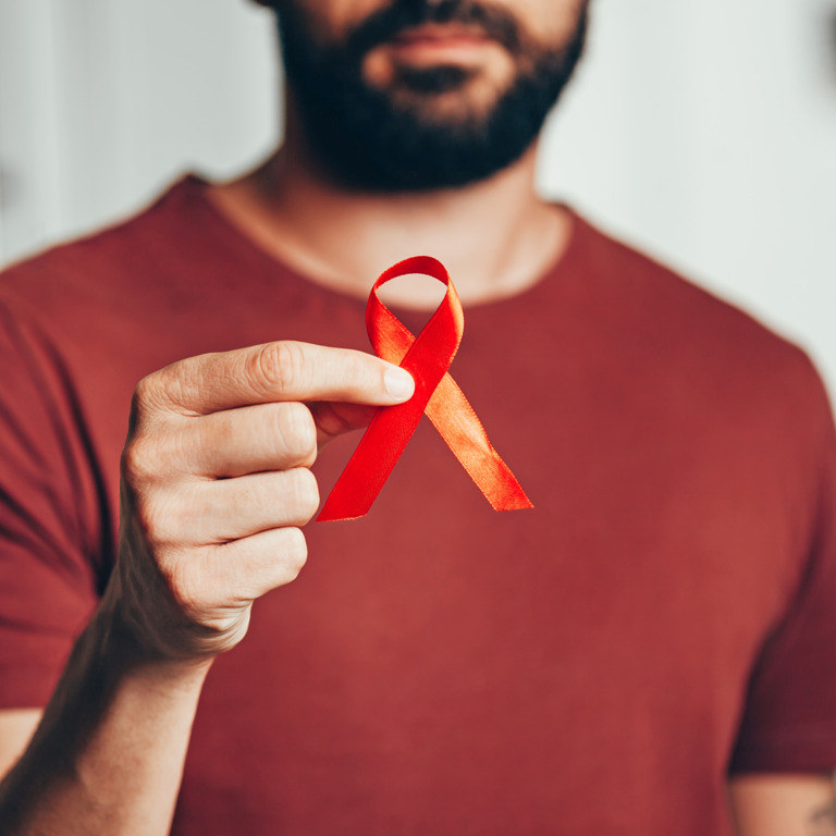 Mann hält eine rote Schleife zur Solidarisierung zum Welt-Aids-Tag in der Hand