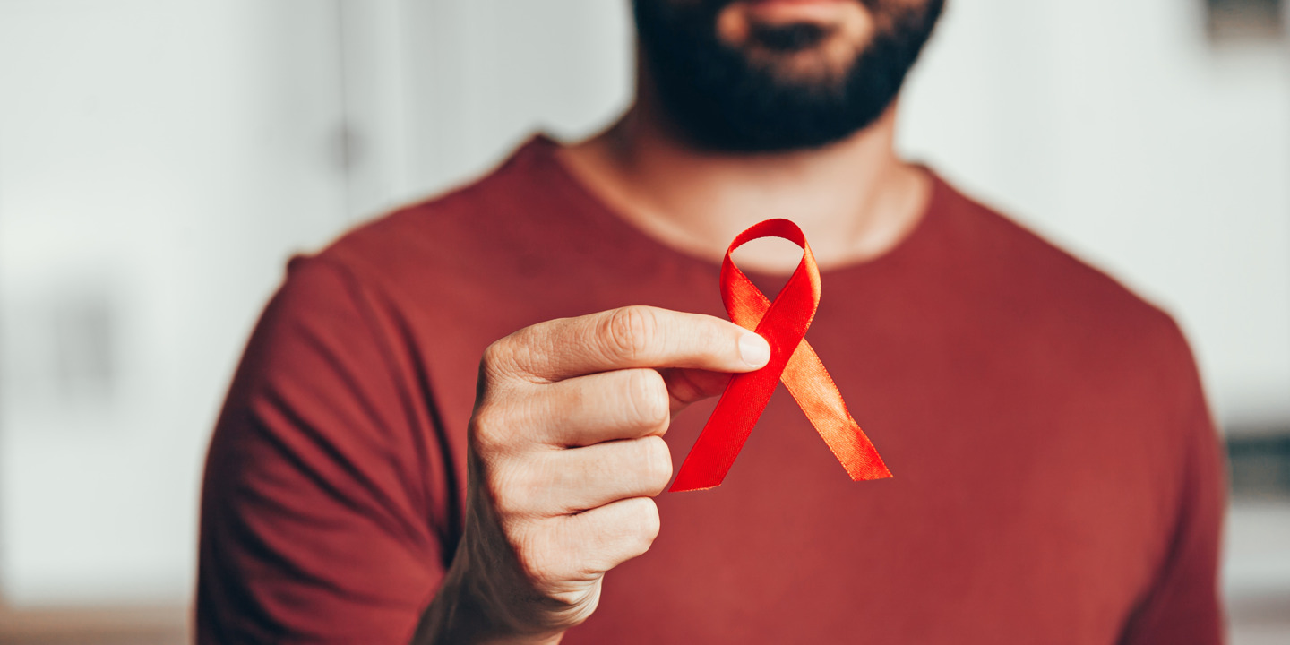 Mann hält eine rote Schleife zur Solidarisierung zum Welt-Aids-Tag in der Hand