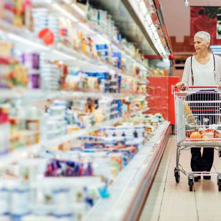 Frau schiebt ihren Einkaufswagen an einer Kühltheke im Supermarkt entlang