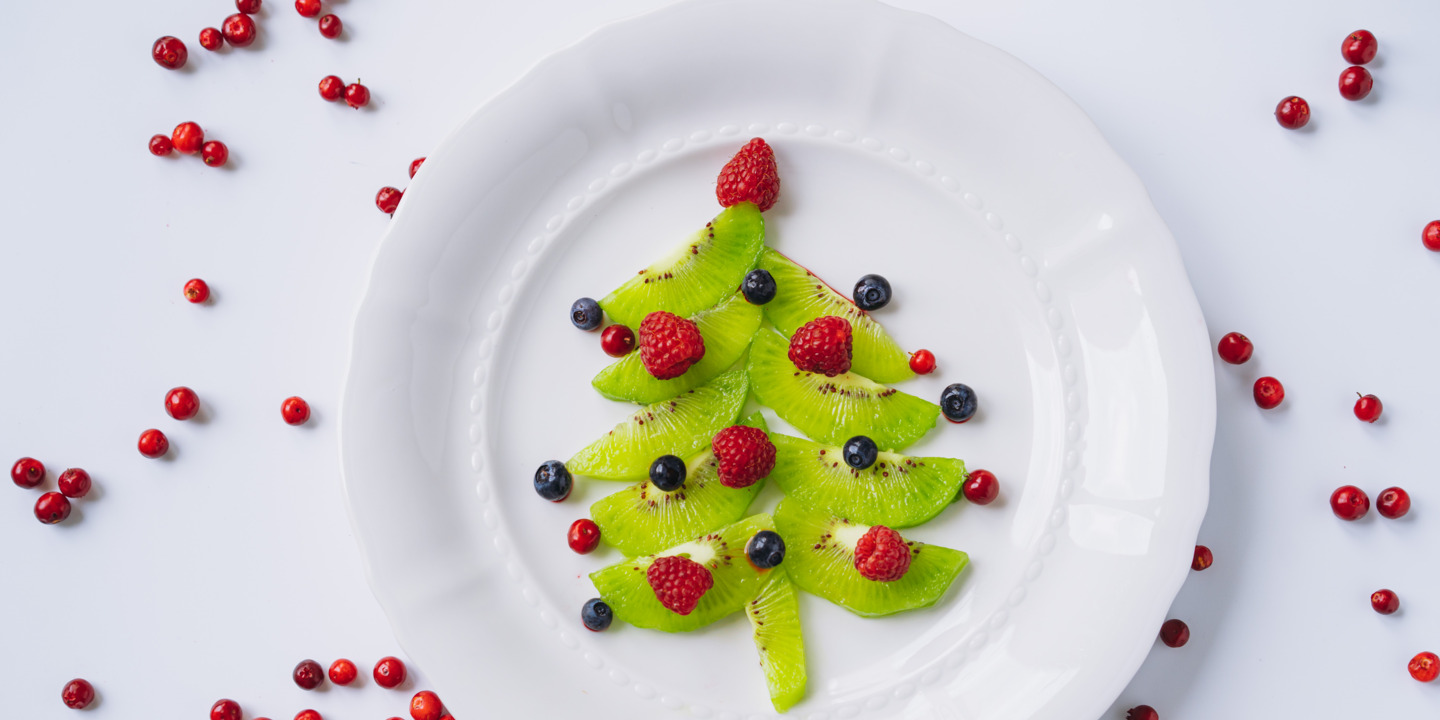 dekorierter Teller mit einem gelegtem Tannenbaum aus Kiwi und Beeren