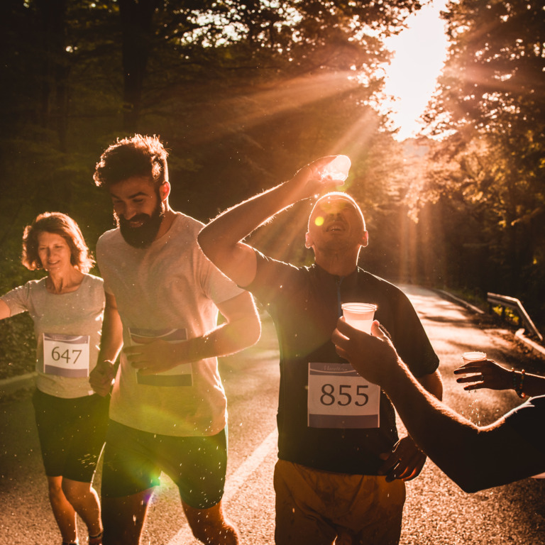 Gruppe von Läufern beim Marathon, ein Mann kippt sich Wasser über den Kopf