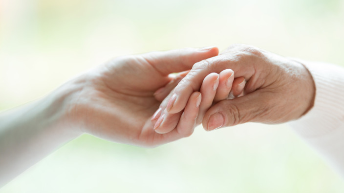 jüngere Frau hält die Hand einer alten Frau