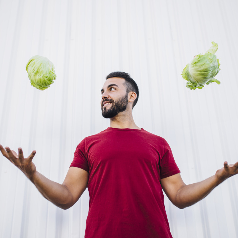 Sportlicher Mann wirft in jeder Hand einen Salat in die Luft