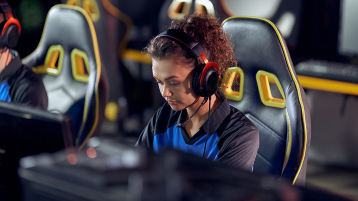 Frau im Gamer-Stuhl und Kopfhörern betreibt E-Sport.