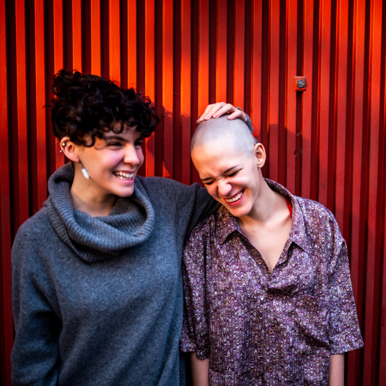 Krebskranke Frau und ihre Freundin stehen lachend nebeneinander