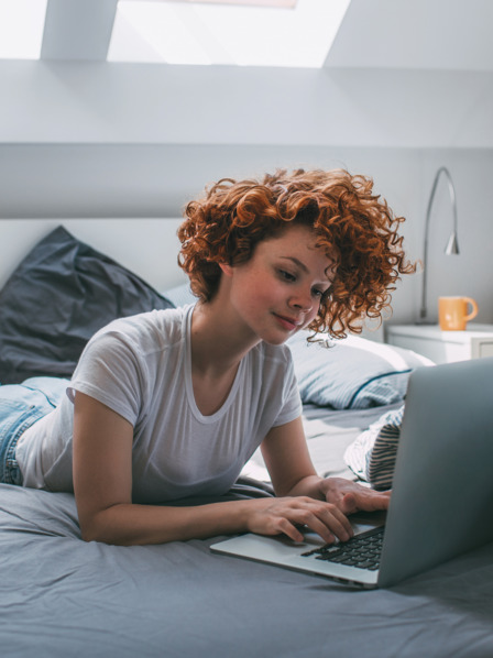 junge Frau liegt auf ihrem Bett und benutzt ihren Laptop