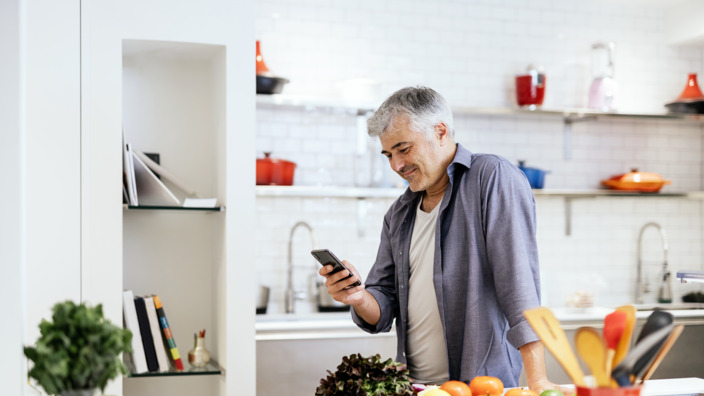 Mann mittleren Alters steht in seiner Küche und prüft eine Angabe seiner Diabetes-App