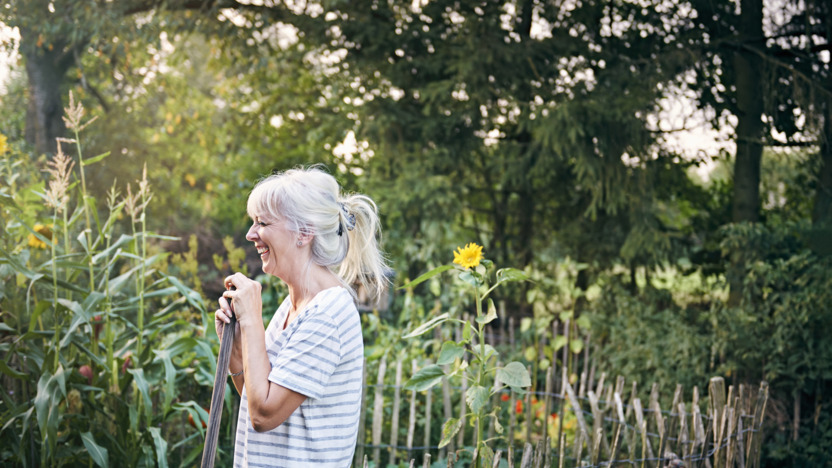 Ältere Frau arbeitet im Garten und lacht.