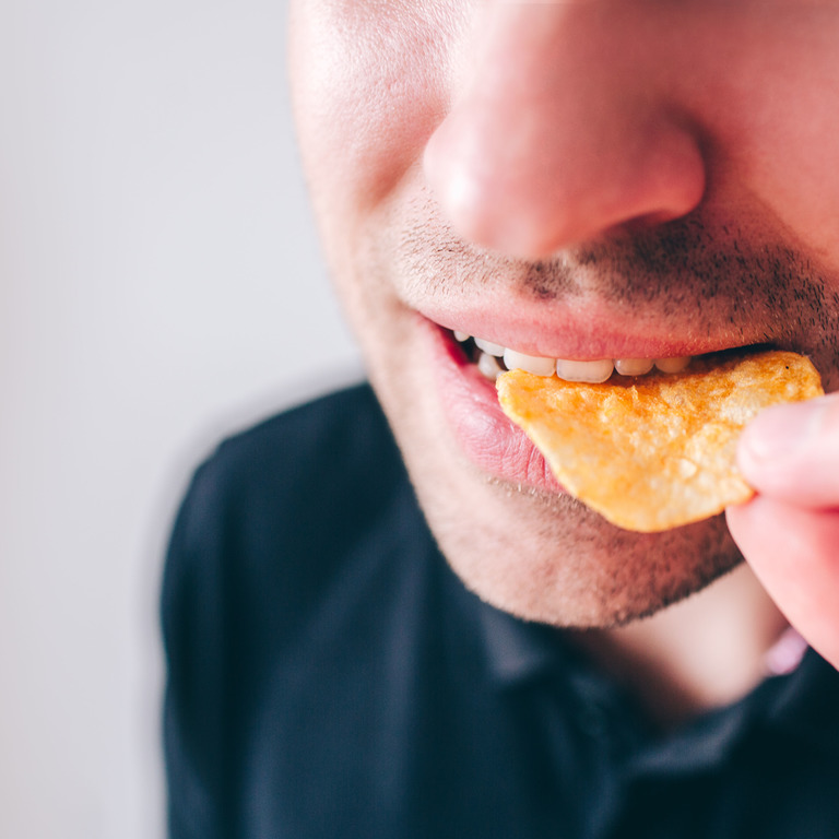 Mann steckt sich Kartoffelchips in den Mund.