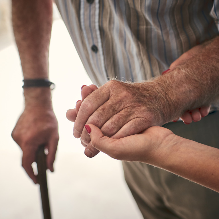 Pflegekraft stützt den Arm eines älteren Mannes mit Gehstock