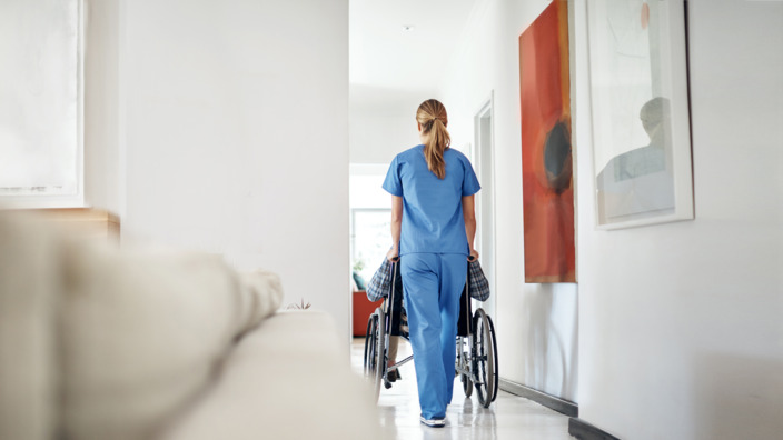 Pflegerin schiebt Rollstuhl über den Gang