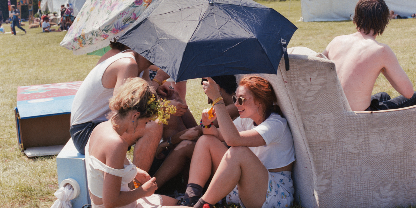 Gruppe junger Leute auf einem Festival schützt sich mit Regenschirmen vor der Sonne.