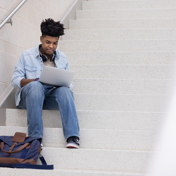 Junger Mann sitzt auf Treppe und schreibt eine Bewerbung.