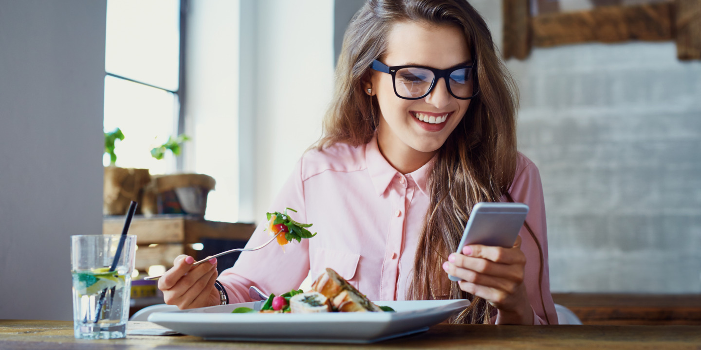 Frau isst Salat und checkt dabei ihr Smartphone