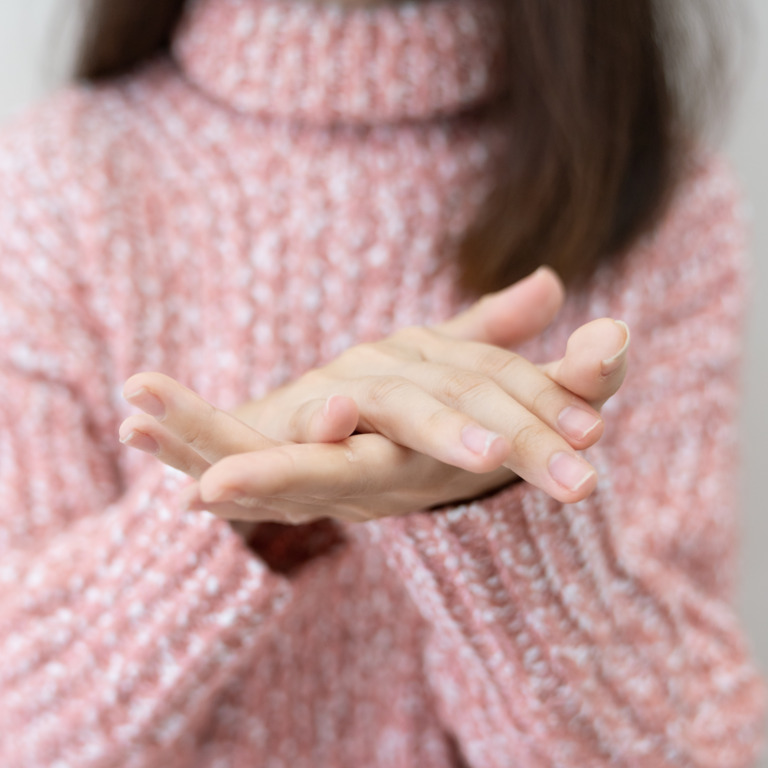 Frau in rosa Pullover zeigt ihre gepflegten Hände.