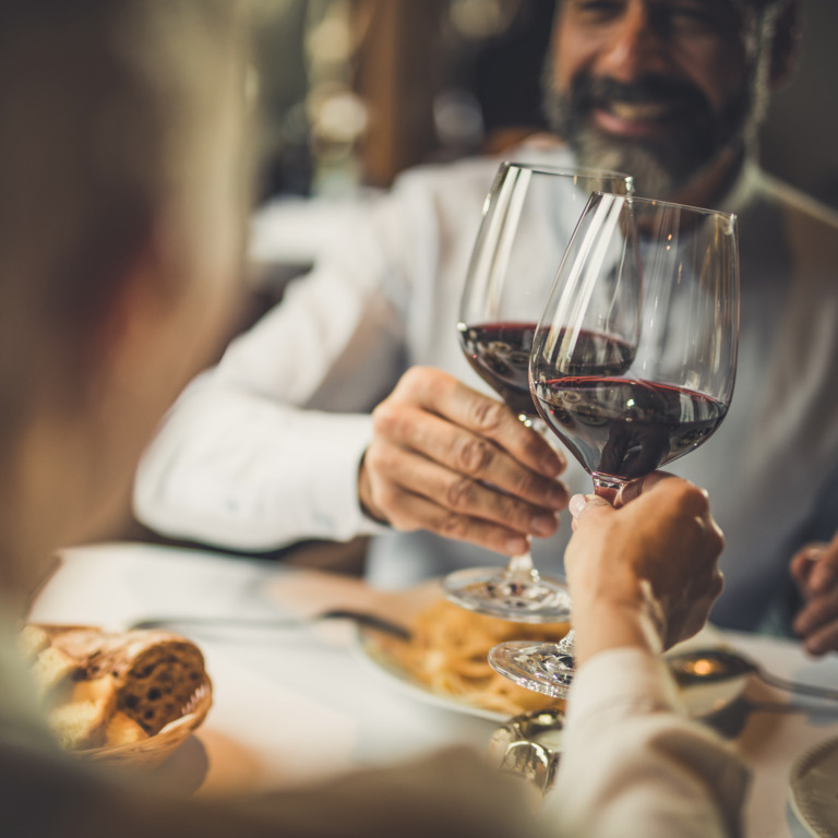 Paar sitzt am Tisch und stößt mit Rotwein an.