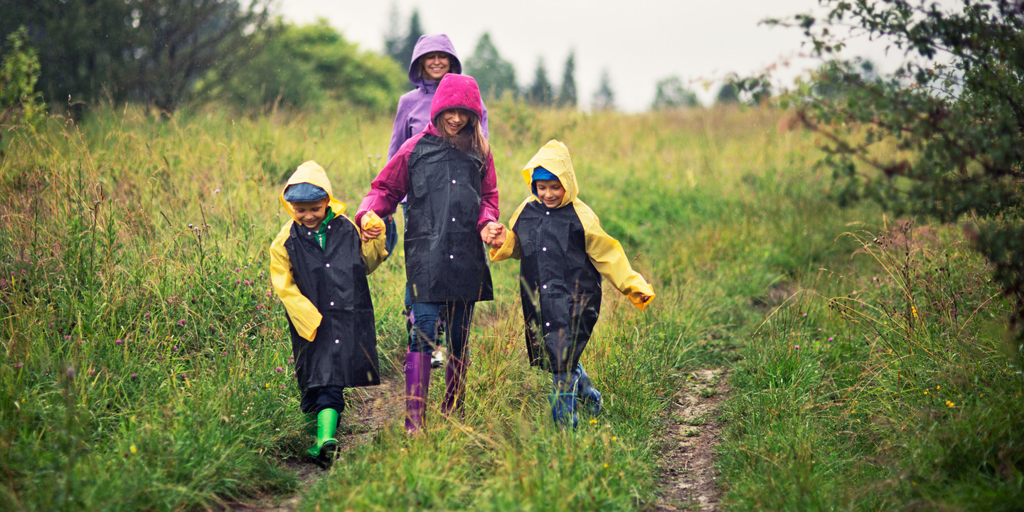Kinder gehen lachend mit Regenmänteln auf einem Feldweg