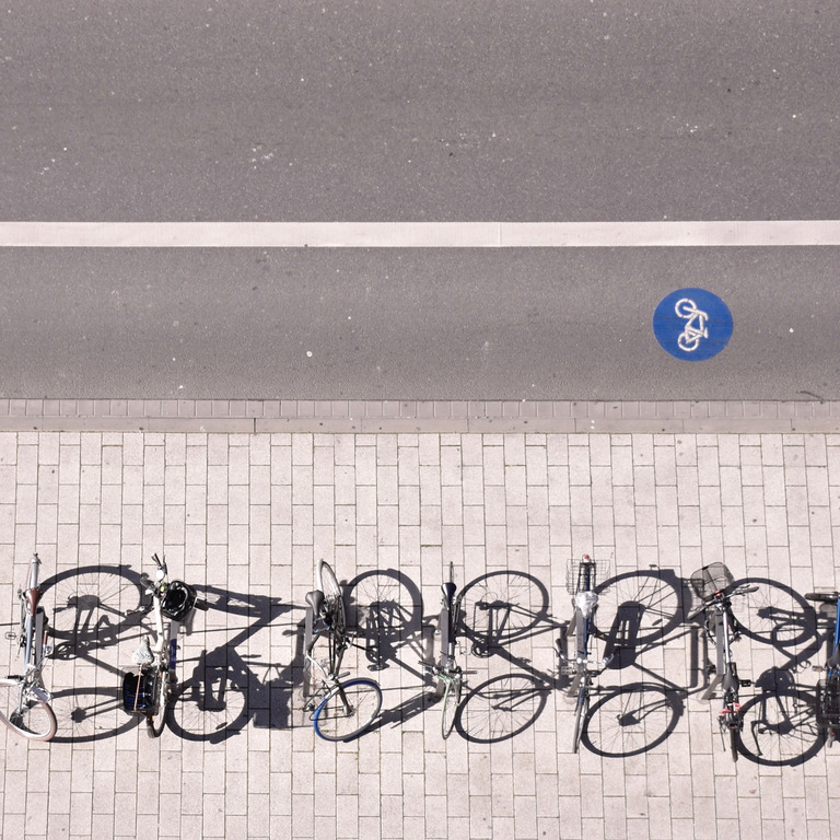Fahrräder und E-Bikes stehen an Fahrradparkplätzen neben einem Fahrradweg.