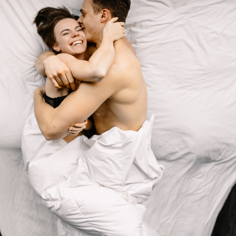 Mann und Frau liegen glücklich im Bett und umarmen sich.