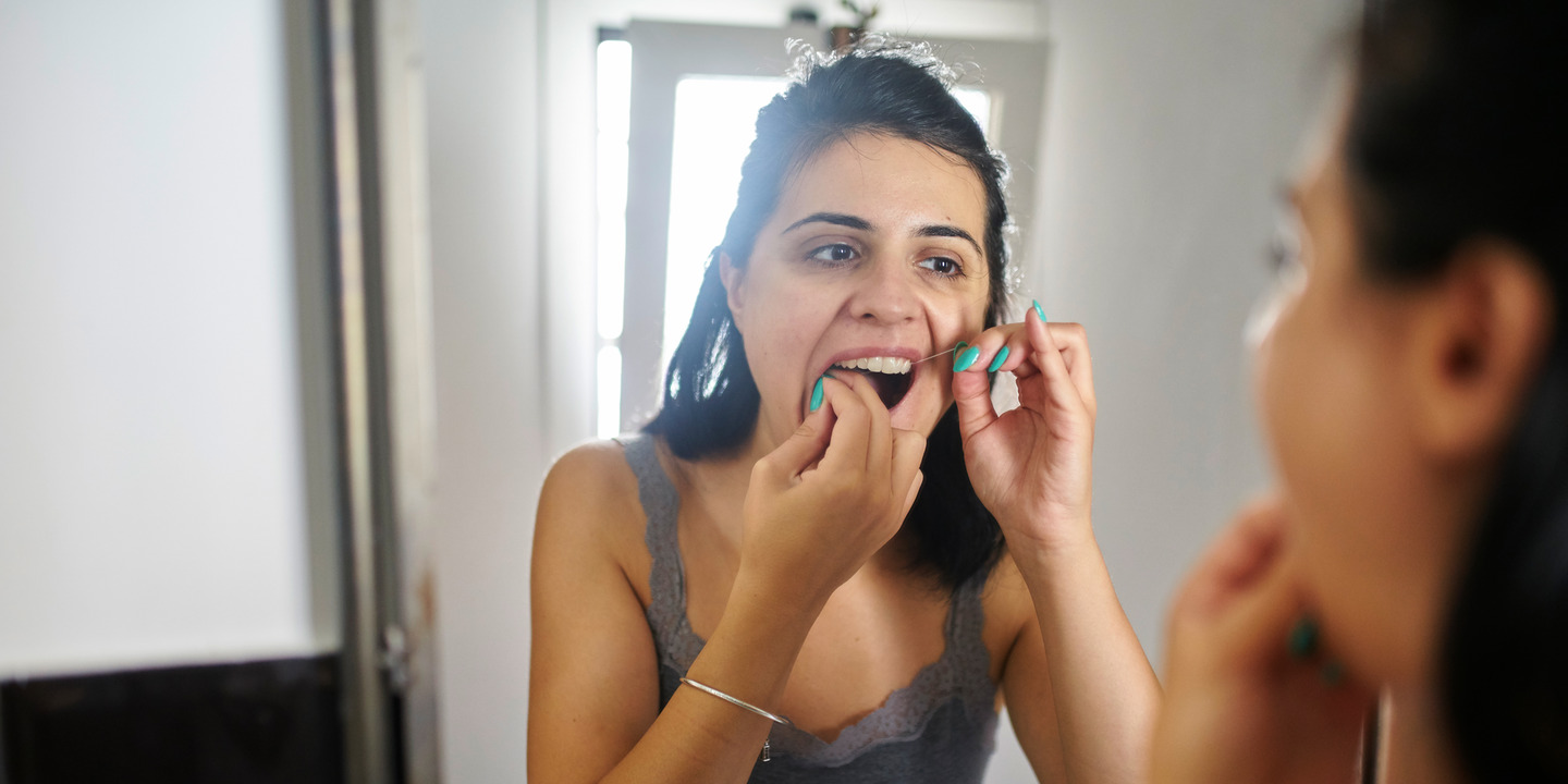 Mädchen reinigt mit Zahnseide am Spiegel ihre Zahnzwischenräume