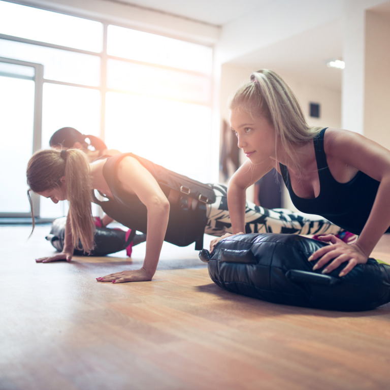 Drei Frauen machen im Fitnessstudio Übungen mit einer Gewichtsweste.