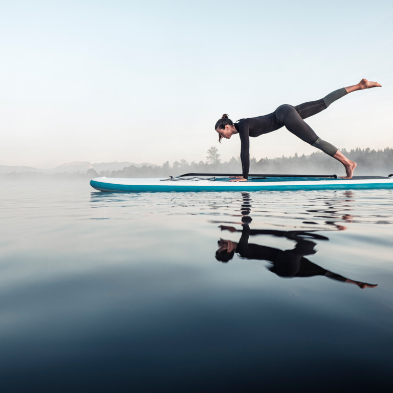 Frau macht Yoga auf einem Stand-up-Paddleboard auf dem See