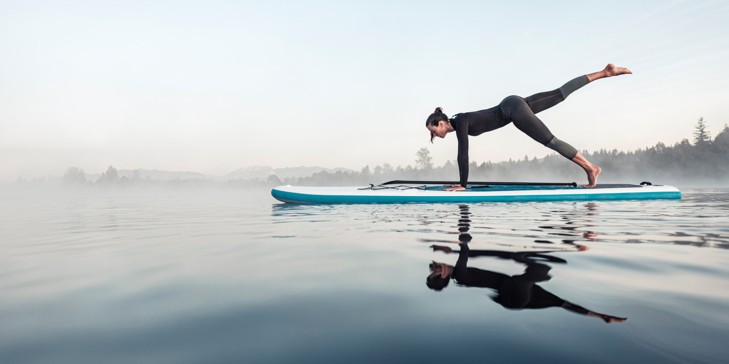 Frau macht Gymnastik-Pose auf einem Surfbrett auf dem Wasser