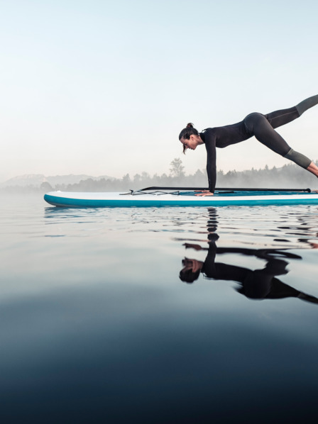 Frau macht Gymnastik-Pose auf einem Surfbrett auf dem Wasser