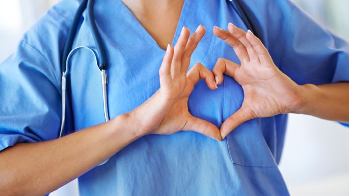 Arzt in OP-Kleidung formt mit seinen Händen ein Herz vor seiner Brust