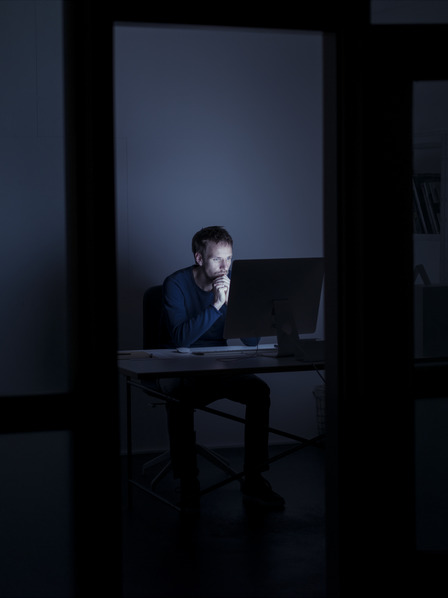 Mann sitzt im dunklen Büro vor dem PC