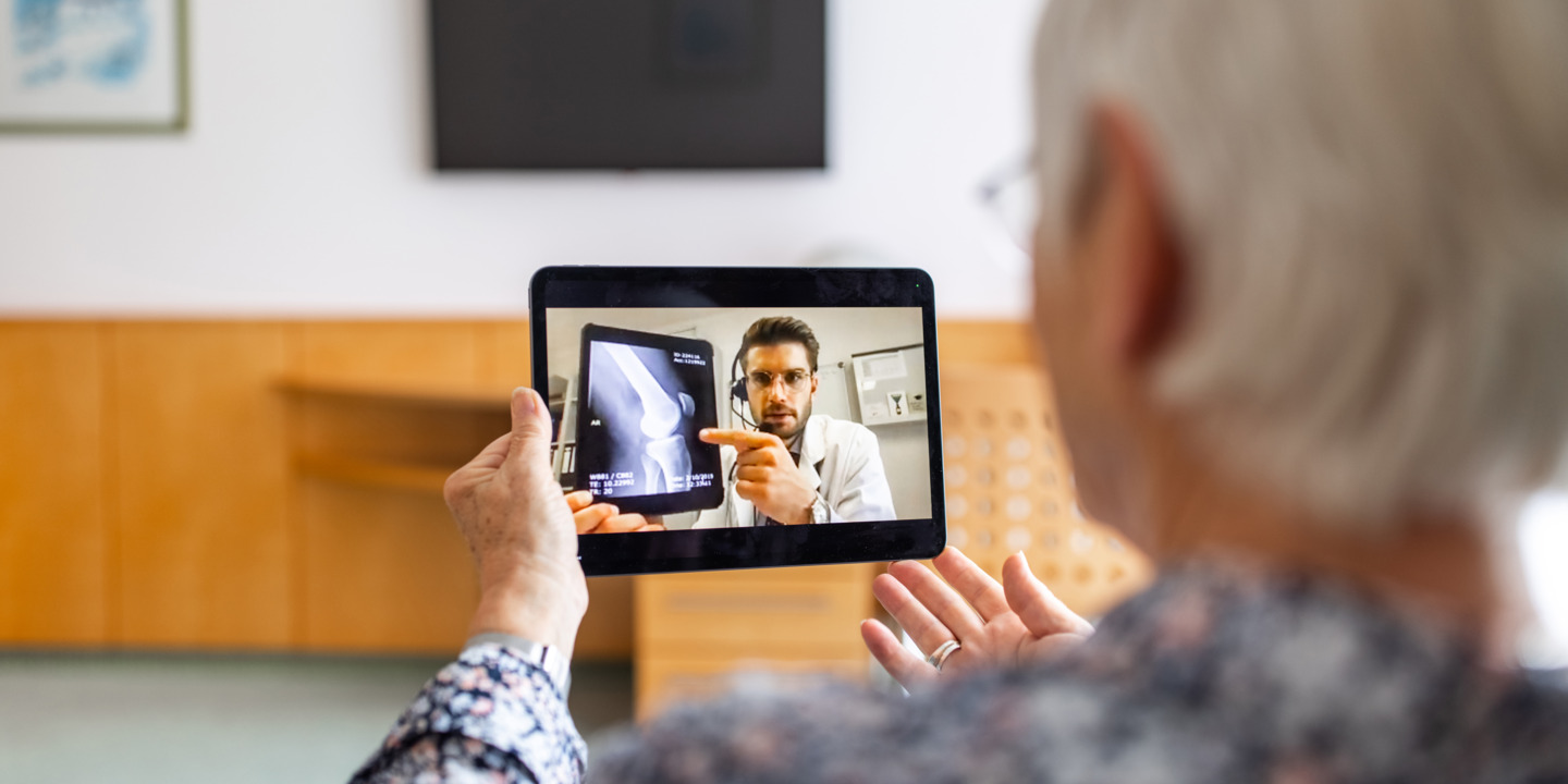 Frau sitzt vor einem Tablet in einer Videosprechstunde mit einem Arzt, der ihr Röntgenbilder erklärt