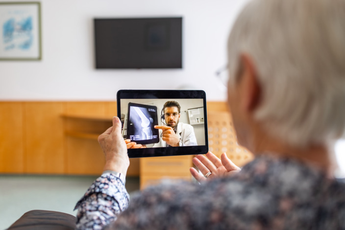 Frau sitzt vor einem Tablet in einer Videosprechstunde mit einem Arzt, der ihr Röntgenbilder erklärt