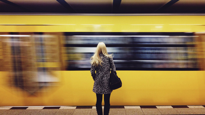 Frau steht am Bahnsteig während eine gelbe U-Bahn vorbeifährt