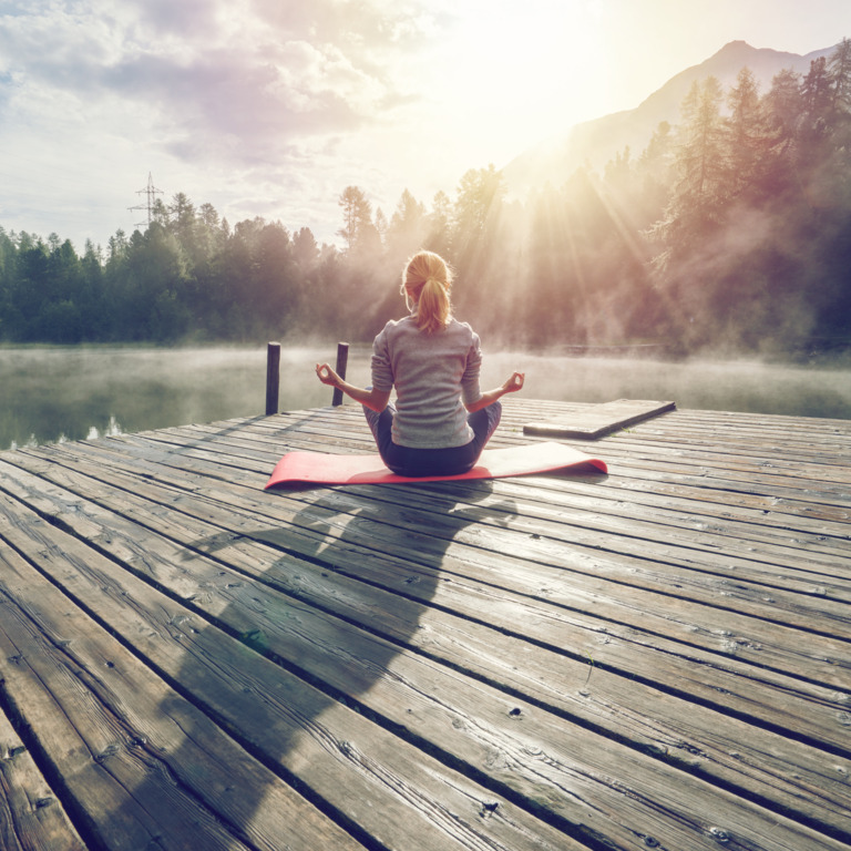 Frau sitzt in Meditationshaltung auf einen Seesteg