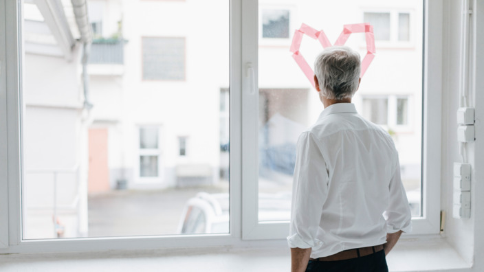 Mann schaut aus einem Fenster, auf das ein Herz geklebt ist