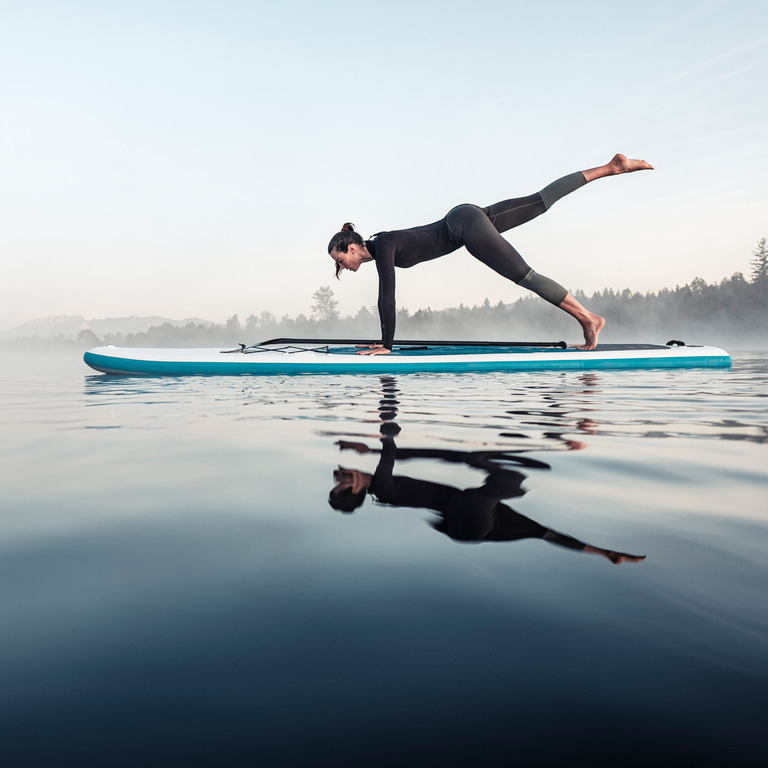 Frau macht Yoga auf einem Stand-up-Paddleboard auf dem See