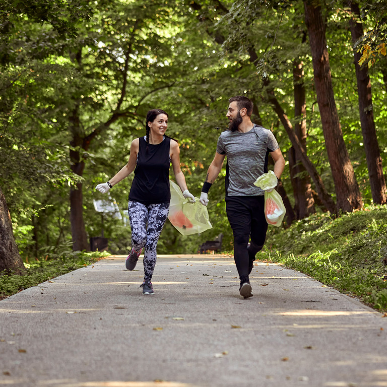 Mann und Frau joggen durch den Wald und sammeln Müll
