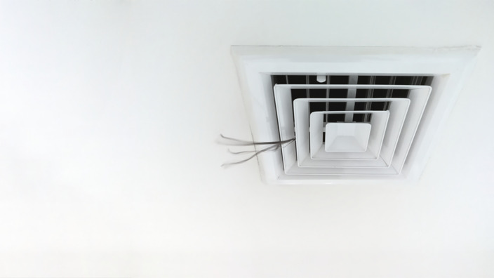 Aus einer Klimaanlage an der Decke eines Büros strömt Luft.