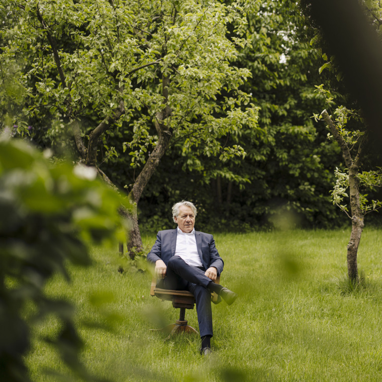 Alter Geschäftsführer sitzt auf einem Holzstuhl im Garten.